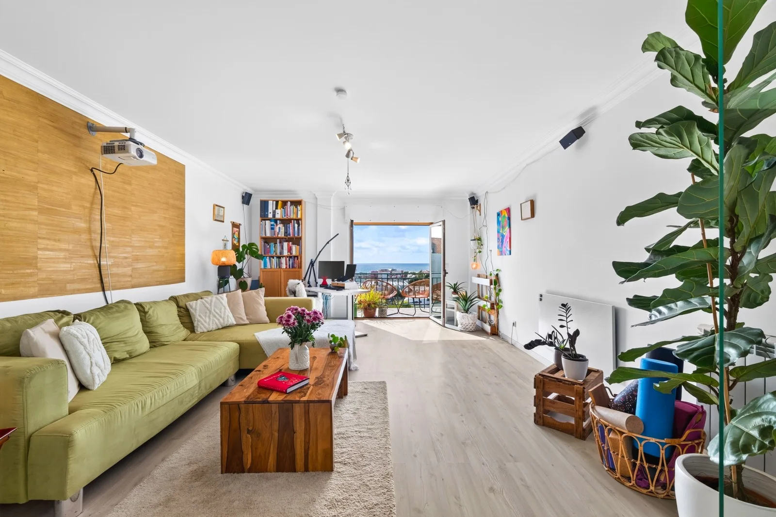 Living room with wooden flooring, green sofa and a bright balcony doorway